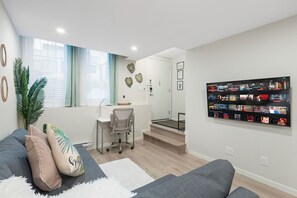 En moderne stue med en grå sofa, et lille skrivebord og stor vægkunst med filmtitler.