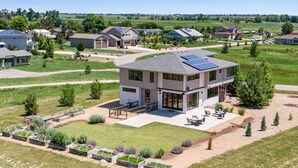 A modern two-story house with a flat roof, solar panels, and a patio with outdoor furniture. - Perfectly Between Boulder - Estes Park! Modern 5-Bedroom House (Longmont)