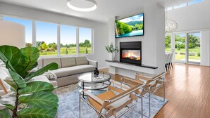A modern living room with a fireplace, a large TV, and a view of the outdoors. - Perfectly Between Boulder - Estes Park! Modern 5-Bedroom House (Longmont)