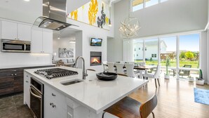 A modern kitchen with a central island, stainless steel appliances, and a dining area with a view of the outdoors. - Perfectly Between Boulder - Estes Park! Modern 5-Bedroom House (Longmont)