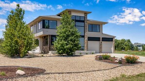 A modern two-story house with a stone facade, large windows, and a gravel driveway. - Perfectly Between Boulder - Estes Park! Modern 5-Bedroom House (Longmont)