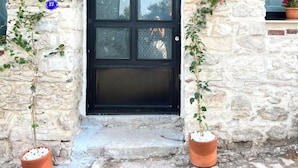 A stone building with a black door, potted plants, and a sign with a 'U' symbol. - NisUrla (Urla)