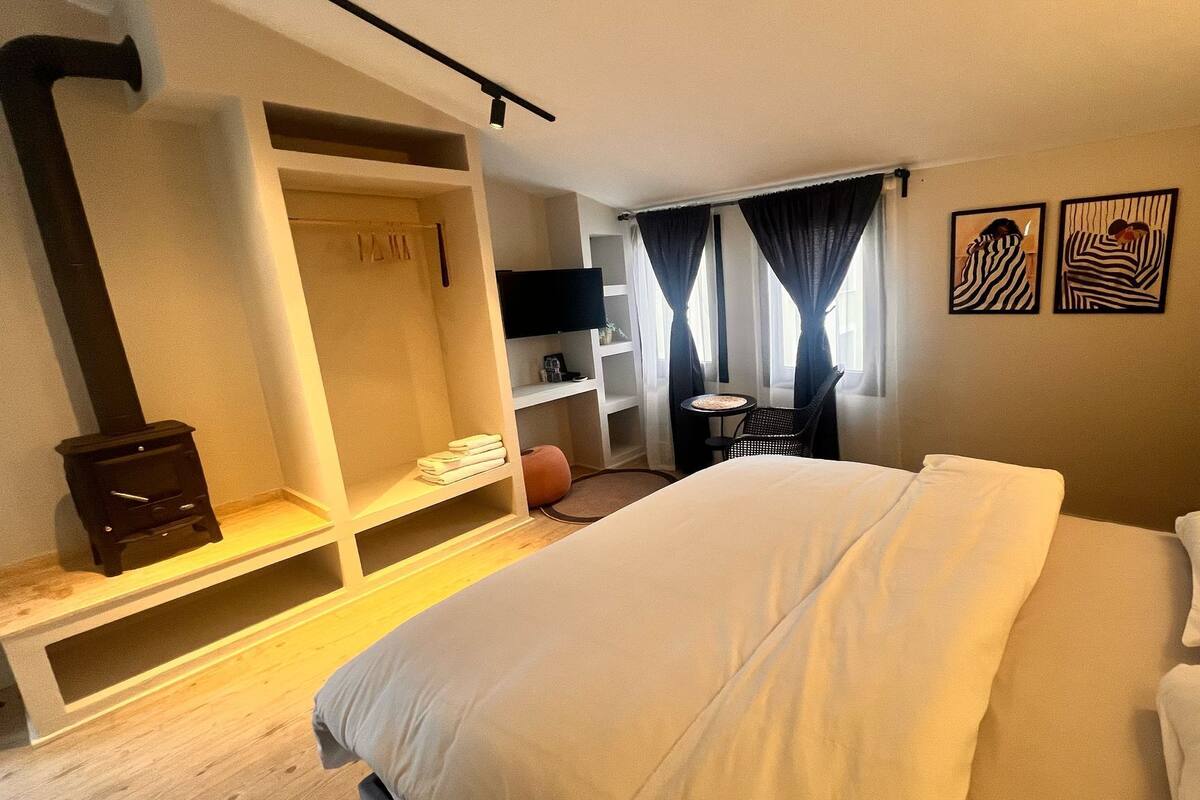 A hotel room with a bed, a wardrobe, a small table, a chair, and artwork on the wall.