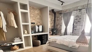A modern bedroom with a wooden floor, a bed with a white duvet, a built-in wardrobe, a TV, and a fireplace. - NisUrla (Urla)
