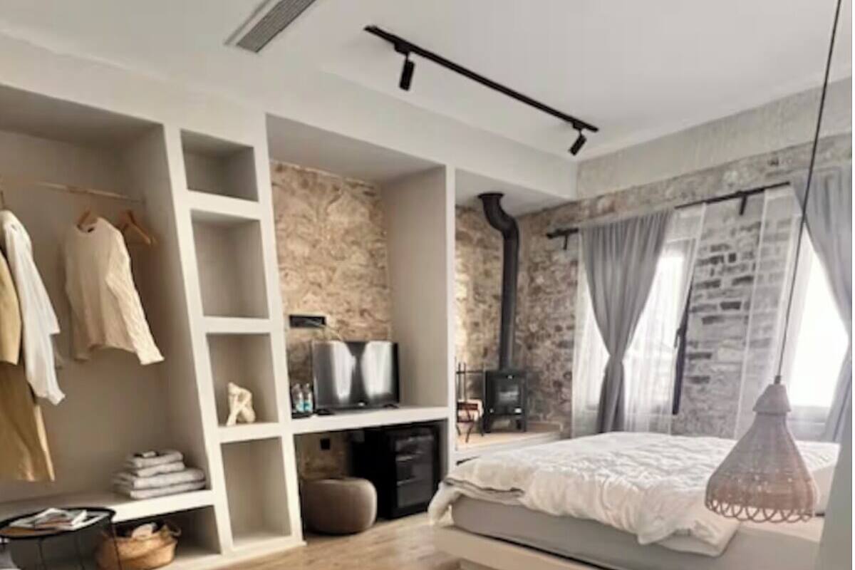 A modern bedroom with a wooden floor, a bed with a white duvet, a built-in wardrobe, a TV, and a fireplace.