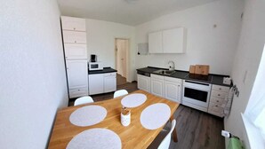 Une cuisine de taille réduite avec des meubles blancs, une table à manger en bois agrémentée de sets de table et un four à micro-ondes.
