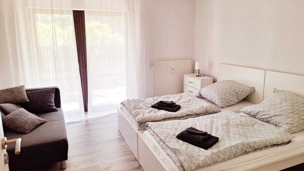 Une chambre avec deux lits, une table de chevet, une chaise et une fenêtre avec des rideaux légers.