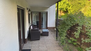 Une terrasse couverte, aménagée avec des meubles en osier, une petite table et une porte-fenêtre coulissante donnant sur un espace intérieur.