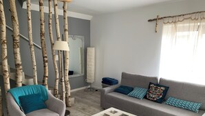 Una sala de estar con un sofá gris, un sillón azul turquesa, una mesa de centro de madera y ramas de abedul como decoración.