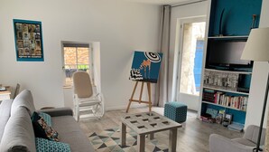 Una sala de estar con sofá, mesa de centro, sillón, estantería y un cuadro sobre caballete.