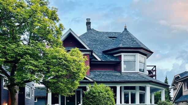 Une maison à deux étages avec une véranda qui fait le tour de la maison, une cheminée et un jardin bien entretenu.