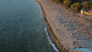 Une vue aérienne d’une plage où se trouvent de nombreuses personnes, avec un ciel dégagé et une mer calme.