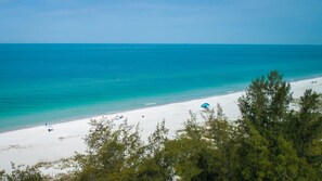 A beach with white sand and turquoise water. There are trees in the foreground.