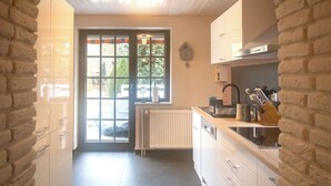 A kitchen with white cabinets, a built-in oven, and a window with a view of greenery outside. - Lütt Heidjer Hus- Stylish oasis of peace. Guests with pets welcome (Buchholz in der Nordheide)