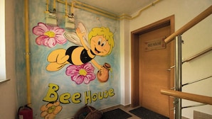 Eine Wandmalerei, die eine Biene zeigt, mit dem Schriftzug "Bee House" und einer Holztür, ebenfalls mit "Bee House" beschriftet.
