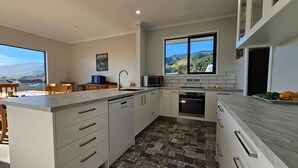 A modern kitchen with a large window, a dishwasher, an oven, and a dining area with a view. - A large and sunny family home close to all the amenities and perfect for exploring Nelson and Tasman (Richmond)