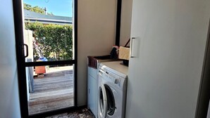 A laundry area with a washing machine and a dryer, a window with a view of a garden and a building, and a door leading to an outdoor area. - A large and sunny family home close to all the amenities and perfect for exploring Nelson and Tasman (Richmond)