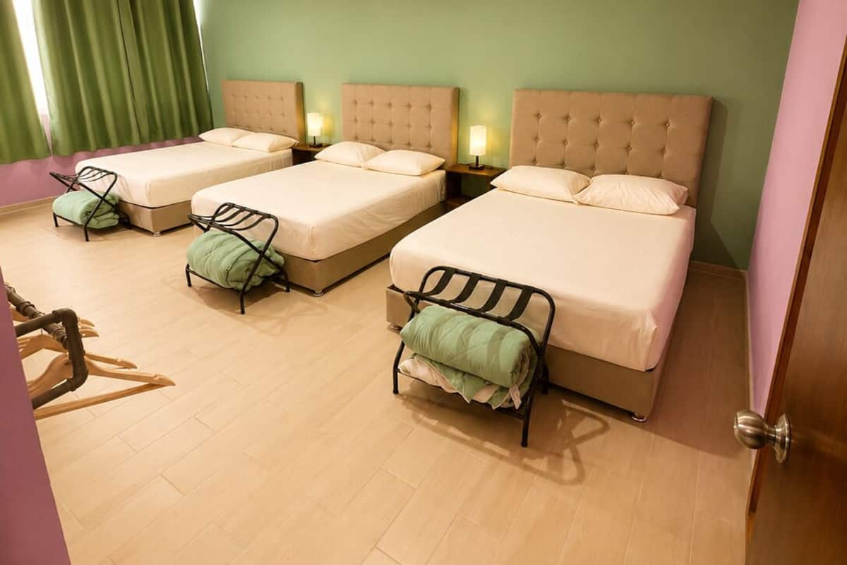 A hotel room with three beds, a wooden chair, and a door.