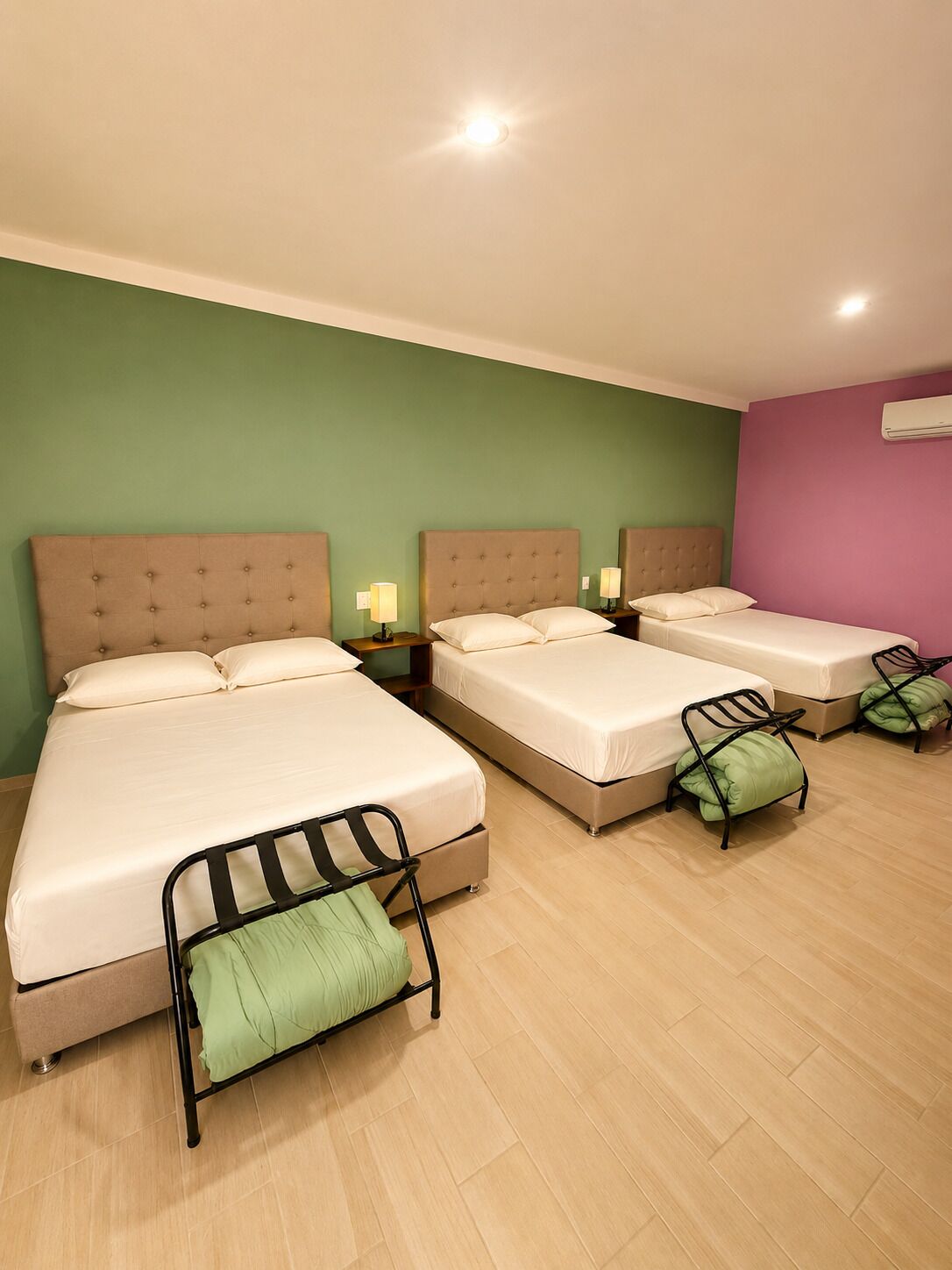 A hotel room with two beds, a green wall, a purple wall, and a wooden floor.