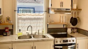 A compact kitchen with white cabinets, a stainless steel sink, a stove, and an oven. - The Garden Alley View (Arcata)
