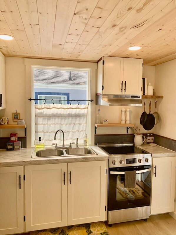A compact kitchen with white cabinets, a stainless steel sink, a stove, and an oven.