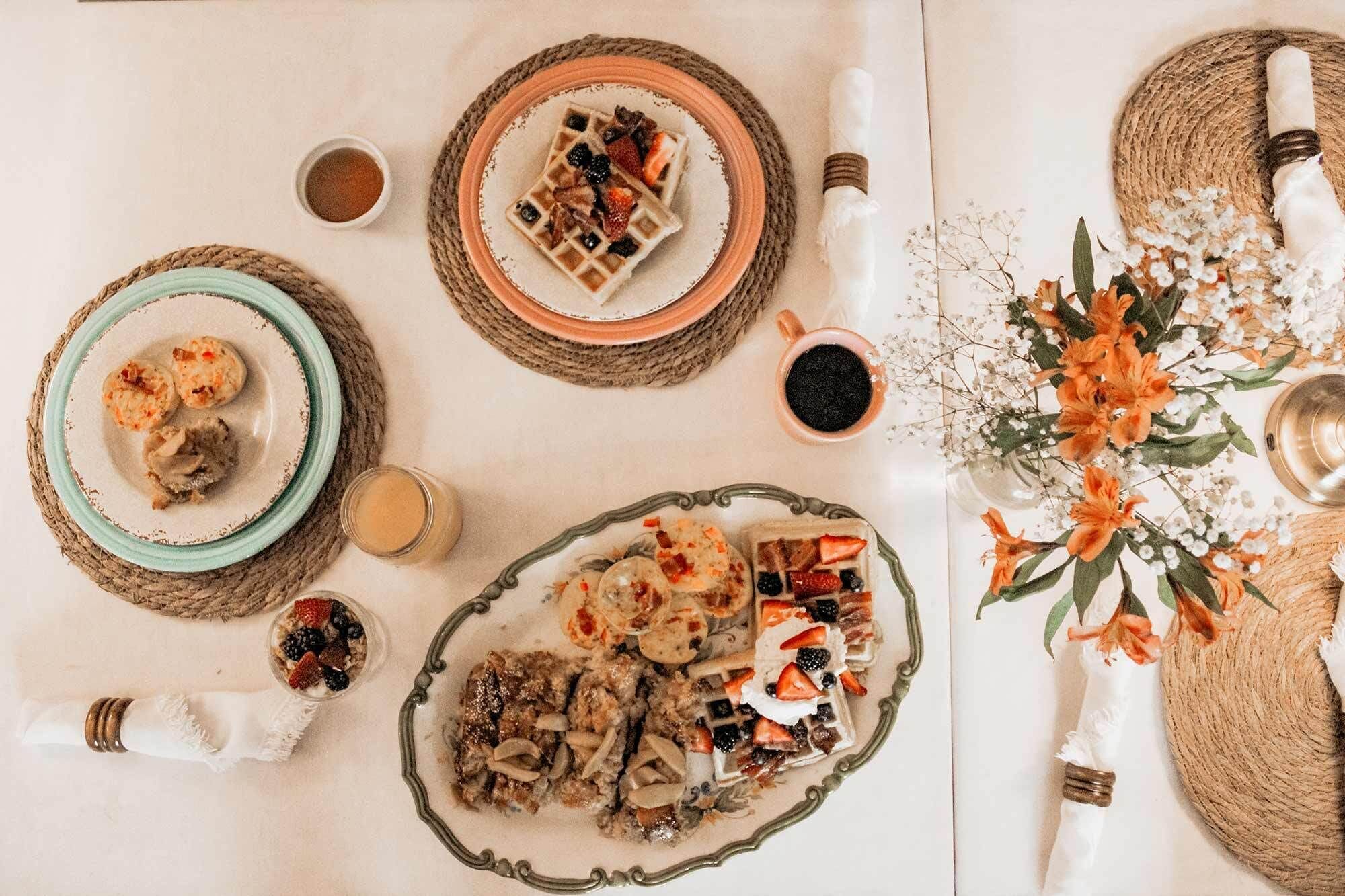 A table set with various dishes, including waffles, pastries, and a bowl of fruit.