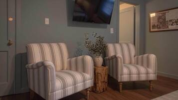 A room with two striped armchairs, a wooden side table with a vase, and a television mounted on the wall.