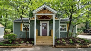 Une petite maison de plain-pied, dotée d’un porche à l’avant, d’un escalier en bois et d’une porte sur laquelle est inscrit le chiffre « 2 ».