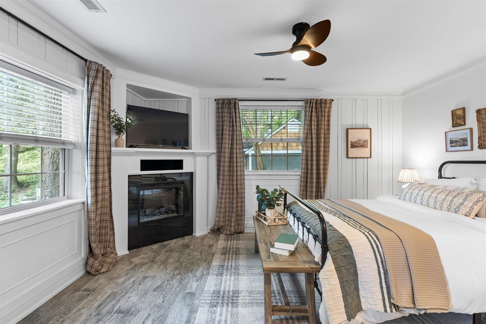 A bedroom with a fireplace, a bed, a bench with a plant, and a ceiling fan.