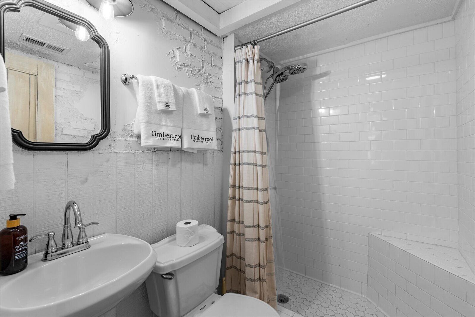 Un baño con lavabo, inodoro y zona de ducha. Hay toallas colgadas en la pared y un espejo sobre el lavabo.