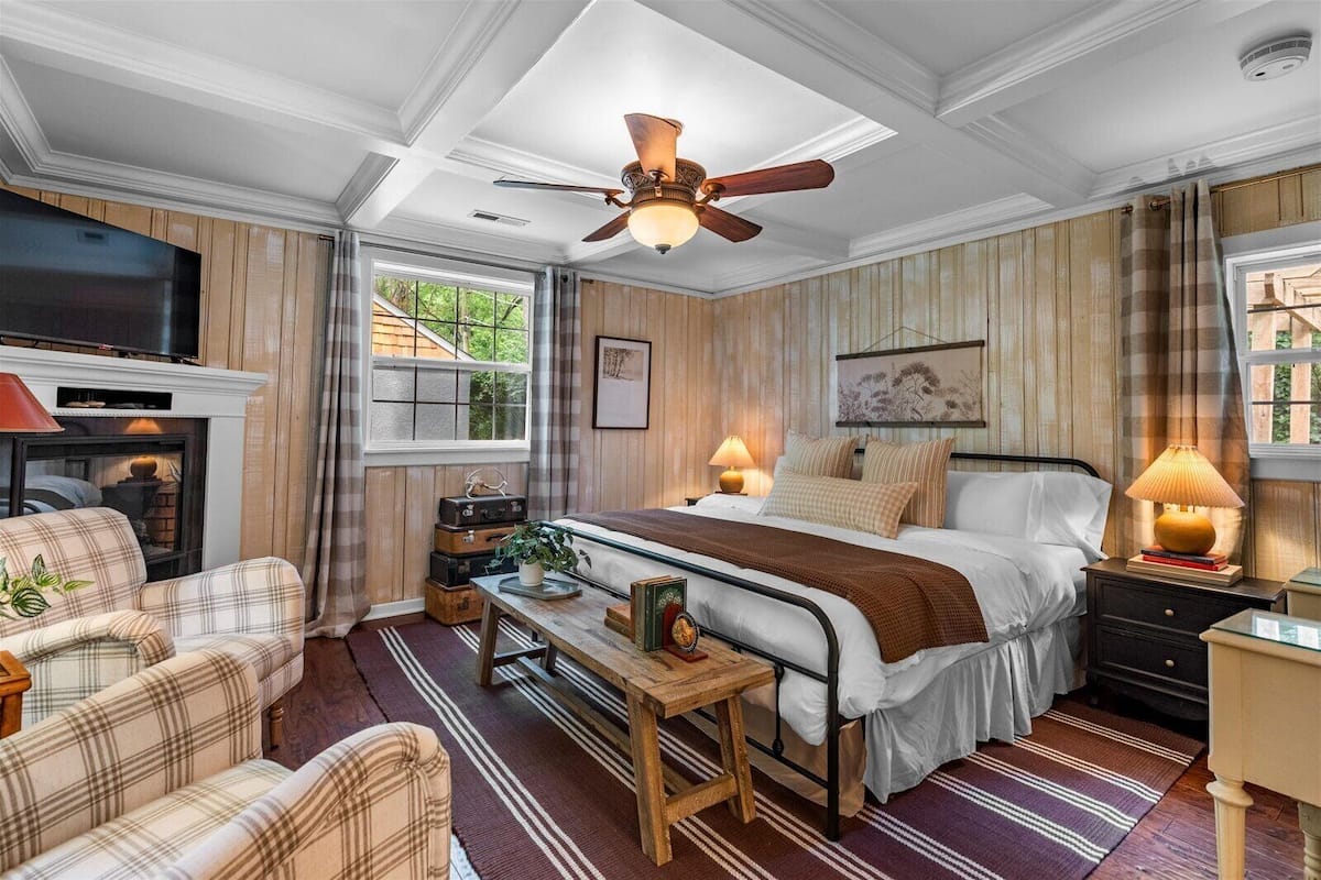 Tunnelmallinen makuuhuone, jossa on sänky, yöpöydät, takka ja kattotuuletin.