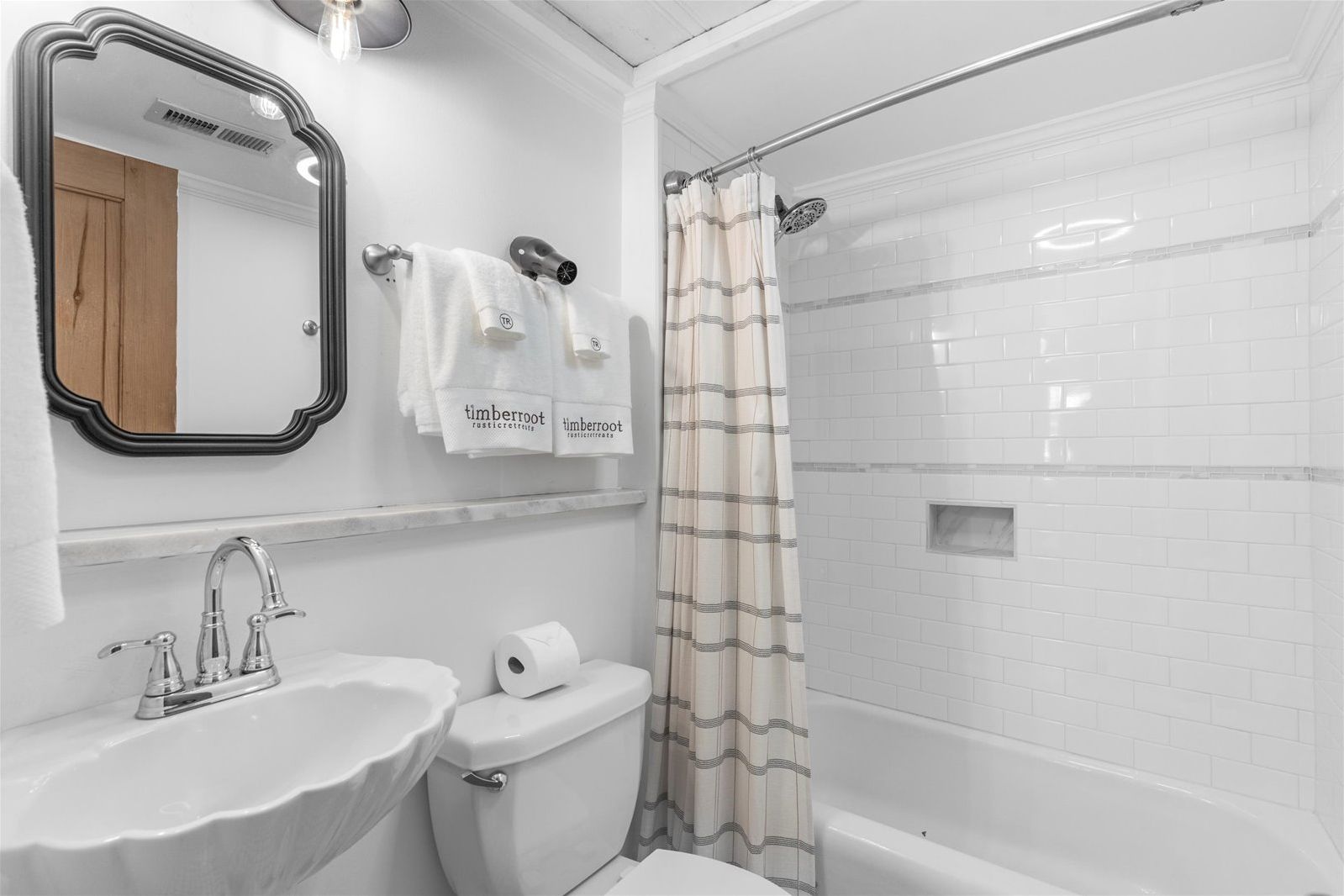 Un baño con lavamanos, inodoro y ducha. Hay toallas colgadas en la pared y un espejo sobre el lavamanos.
