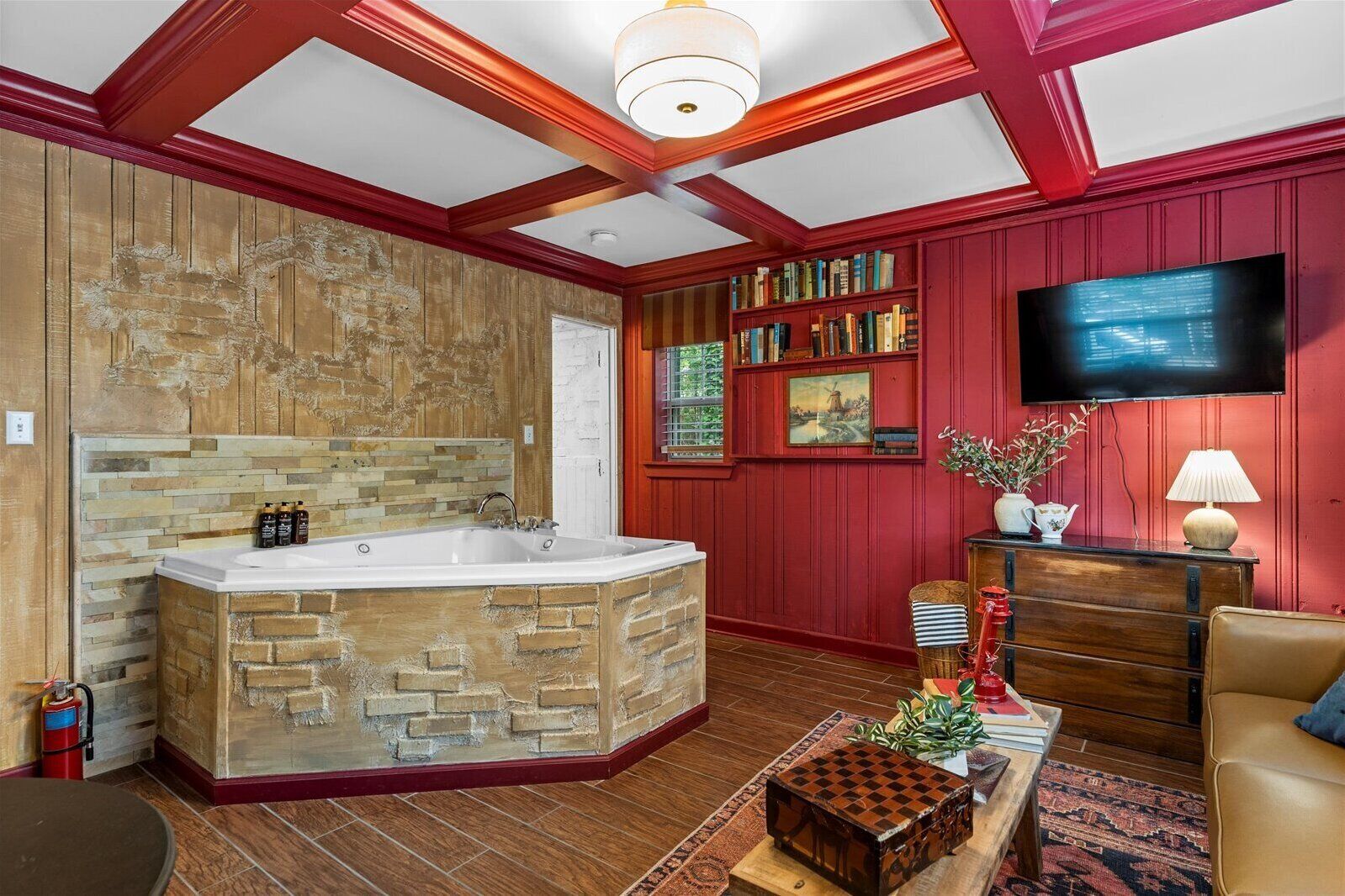 Una habitación con una bañera de piedra, estanterías, un televisor y una pared roja.