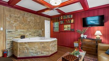 Una habitación con una bañera de piedra, estanterías, un televisor y una pared roja.