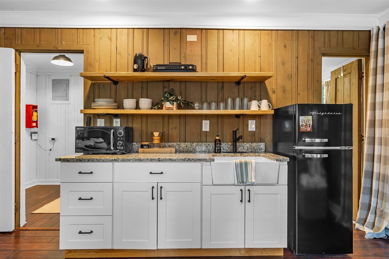 A modern kitchen with white cabinetry, a black refrigerator, and wooden shelves above the counter.