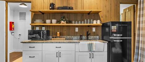 A modern kitchen with white cabinetry, a black refrigerator, and wooden shelves above the counter.