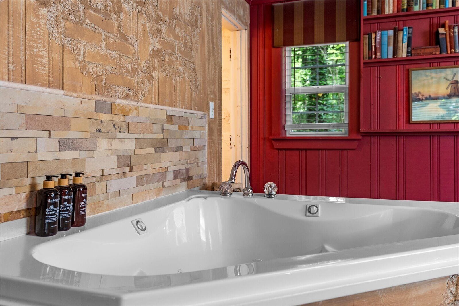 A bathroom with a stone mosaic wall, a white bathtub, and a red wall with a window.