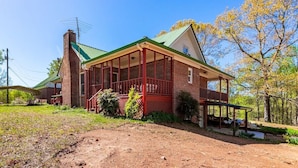 A two-story brick house with a green roof, a covered porch, and a chimney.