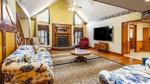 A spacious living room with a high ceiling, a fireplace, a television, and a staircase leading to an upper level.