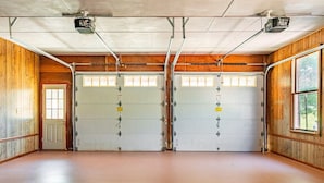 A garage with two large white garage doors, wooden walls, and a concrete floor.
