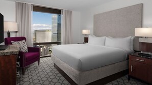 A hotel room with a large bed, a desk, a chair, and a view of a cityscape.