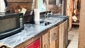 A compact kitchen with a microwave, sink, and red storage drawers.