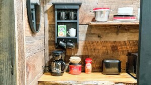 A compact kitchen with a wooden countertop, a coffee maker, a toaster, and a shelf with mugs and containers.