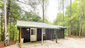 A small, single-story cabin with a metal roof, a front door, and a porch area.