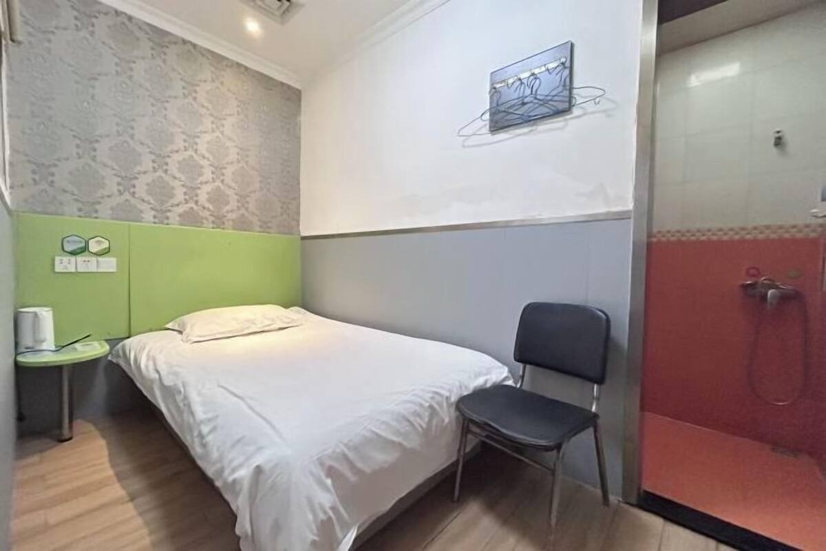 Habitación de hotel con cama, una silla, una mesita de noche con lámpara y zona de ducha.