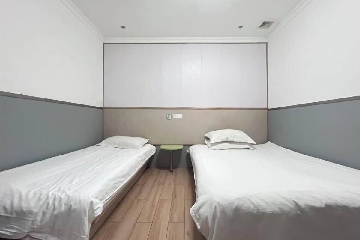 Una habitación de hotel pequeña y sencilla, con dos camas individuales, una mesita y un televisor montado en la pared.
