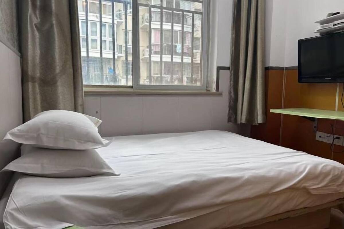 Habitación de hotel con cama, ventana con cortinas, televisor sobre un mueble y vista a edificios.