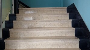 Unos escalones de mármol color beige con bordes negros que conducen a una plataforma.