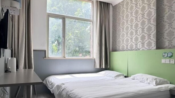 Habitación con dos camas, una ventana con cortinas, un cabecero verde y un papel tapiz estampado en la pared.
