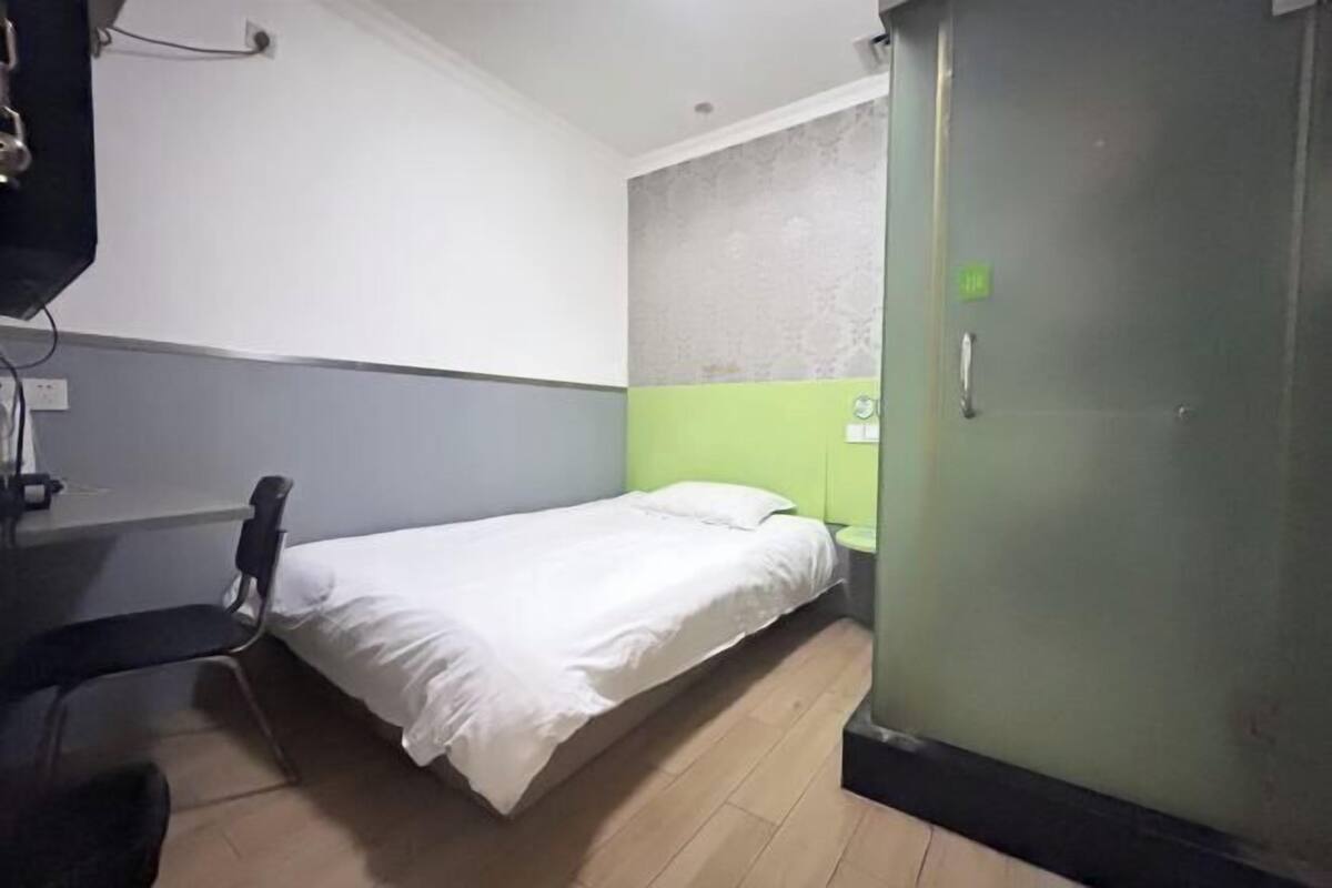 Una habitación pequeña con cama individual, una pared verde decorativa, un escritorio con silla y un armario.